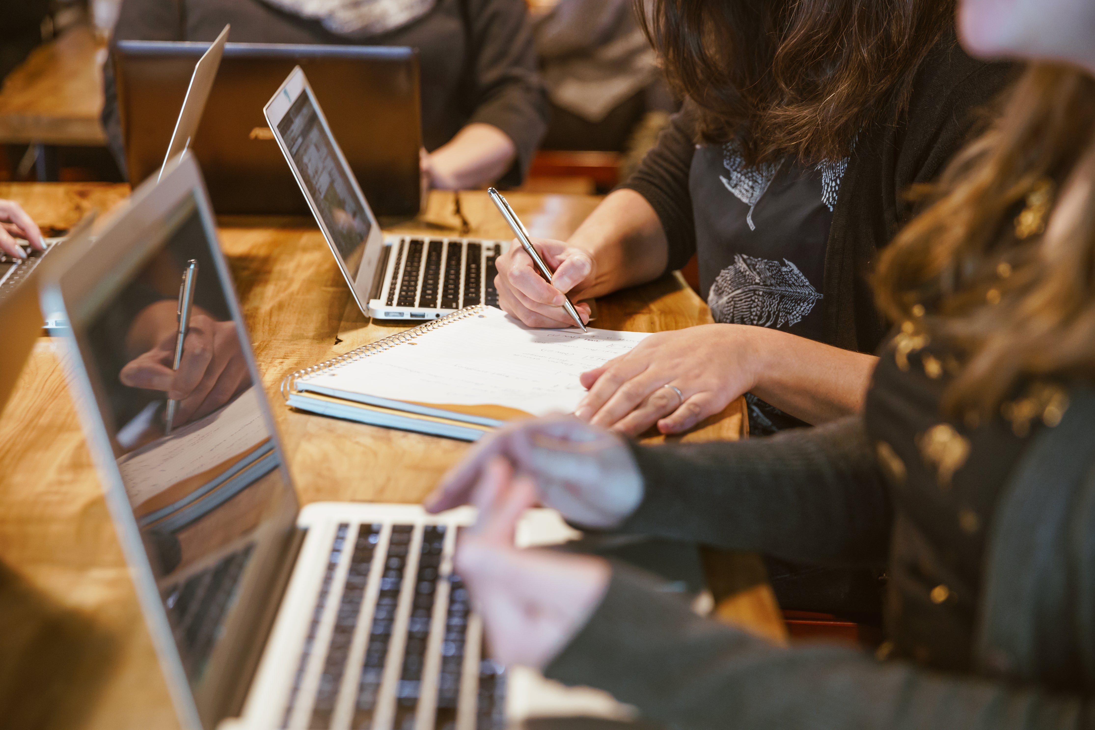 Two people sat at a table with laptops and notebooks performing automation testing
