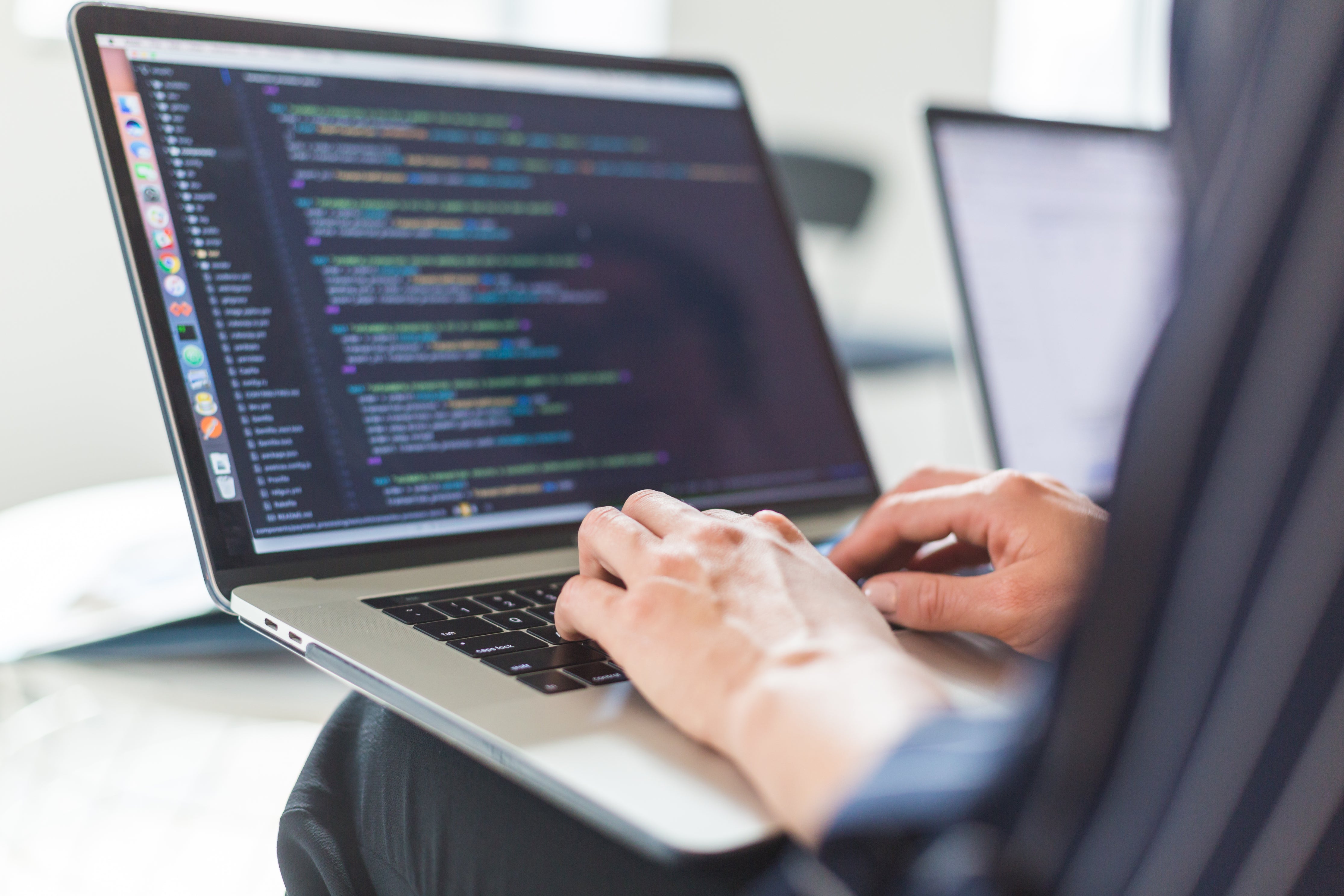 A developer resting a laptop on his knees whilst working on code for a bespoke CRM platform.